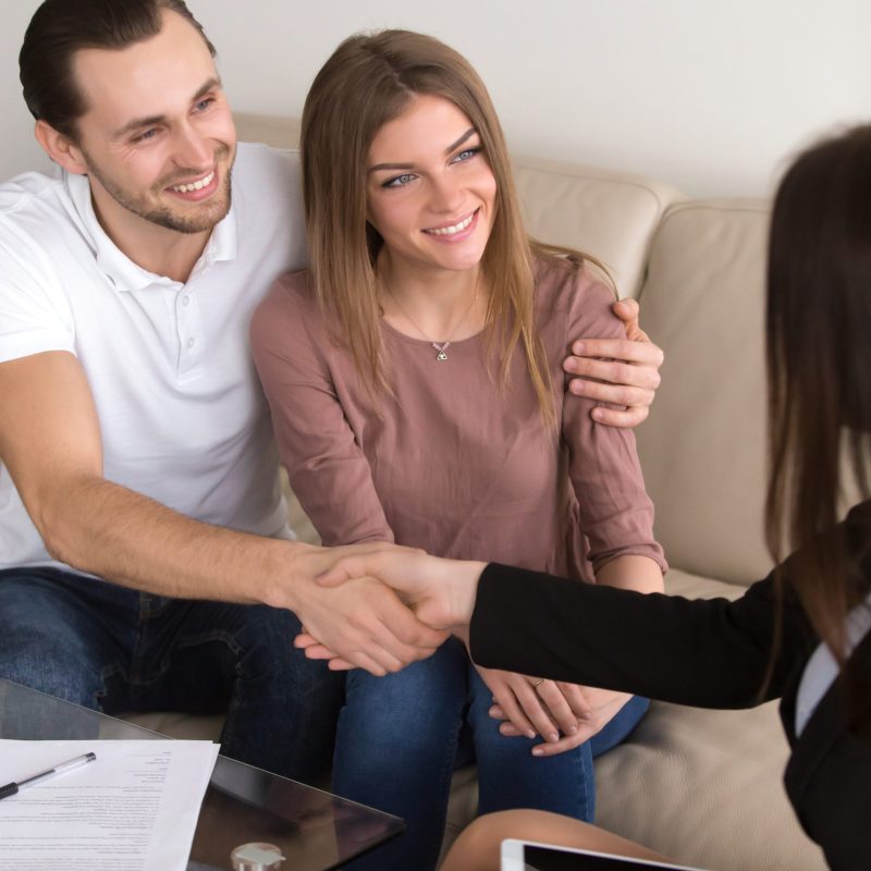 Happy cheerful couple shaking hands with female travel manager or bank worker after signing contract, personal insurance agreement, deal with advisor, lawyer or consultant, vertical