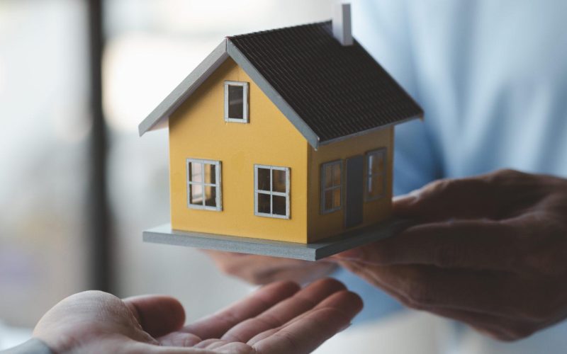 A housing salesman holds a model of a house and sends it to customers as an example, a sample house project where a salesperson advises customers. The concept of selling houses in the project.